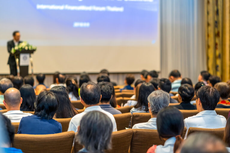 Back side of audience listening the Speaker with podium on the s